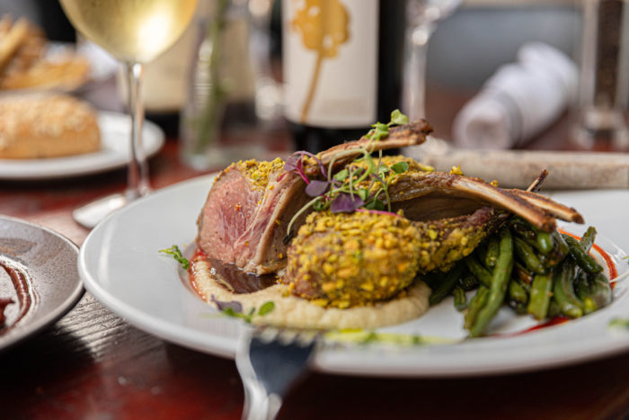 Plated pistachio crusted rack of lamb with green beans, parsnip puree served with wine.