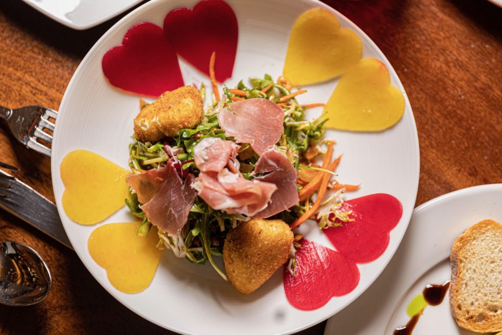 Colorful salad with prosciutto and warm goat cheese, plated with red and yellow beets in the shop of hearts