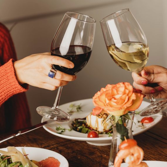 Two people toasting red and white wine over dinner