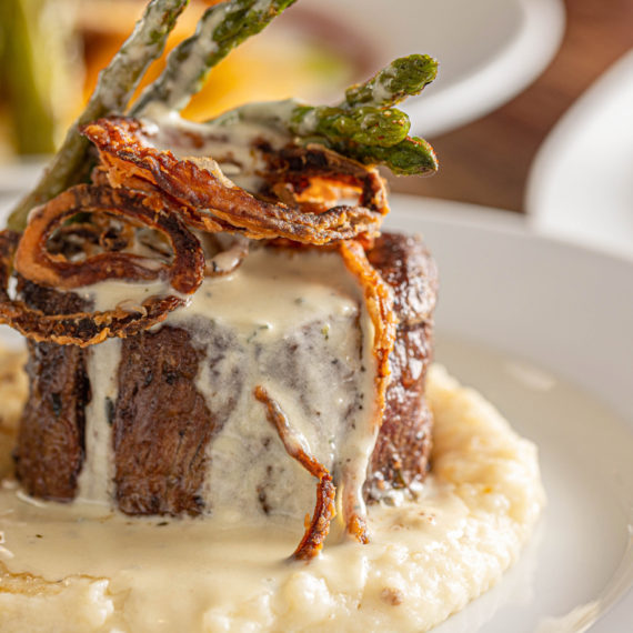 Filet mignon with creamy sauce, fried onions, and asparagus over mashed potatoes