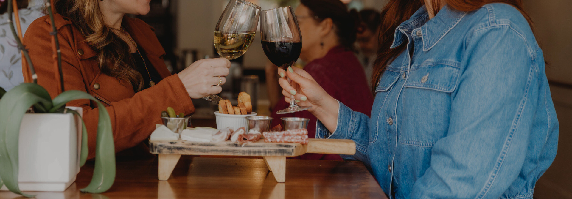 Two women clinking wine glasses over a charcuterie board