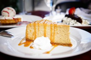 Slice of caramel-drizzled cheesecake with whipped cream, served on a white dessert plate.