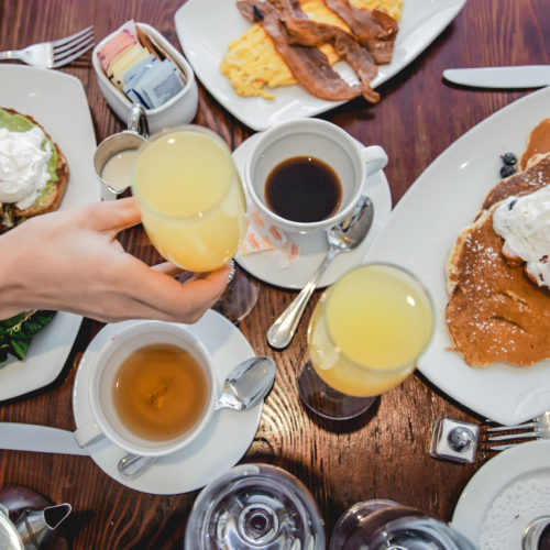 Brunch table with mimosas, pancakes, eggs, bacon, and coffee