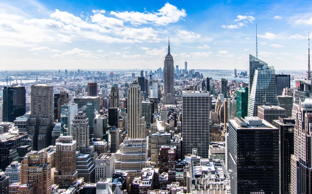 Daytime skyline of Manhattan with Empire State Building and skyscrapers under blue sky.