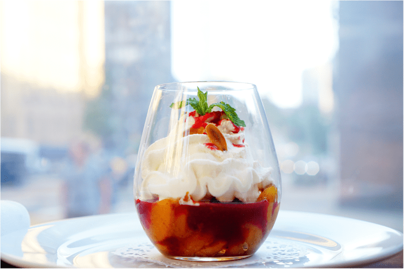 Peach melba layered with peaches and whipped cream in glass with mint garnis