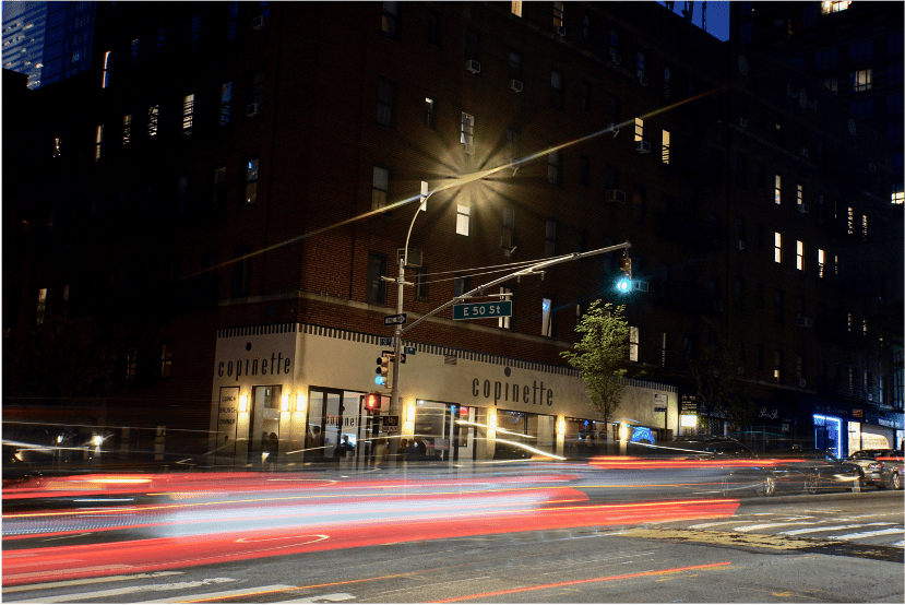 Exterior of Copinette restaurant at night with light trails from passing cars