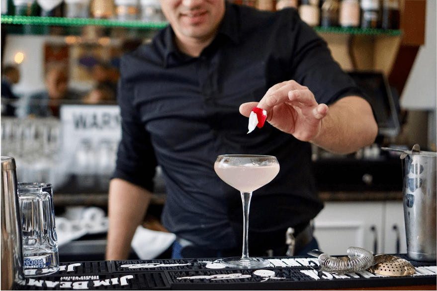 Bartender garnishing pink cocktail with flower petal at the bar