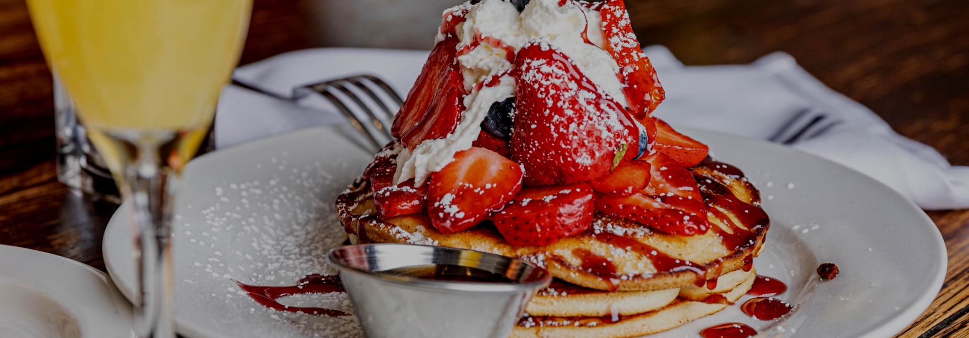 Pancakes topped with strawberries, whipped cream, and syrup drizzle.