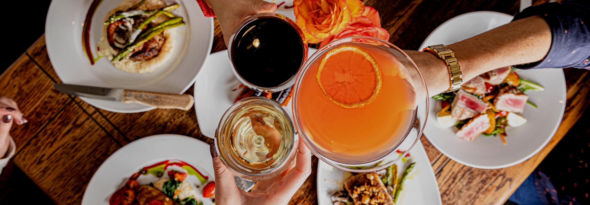 Three cocktails raised in toast over colorful plated dishes