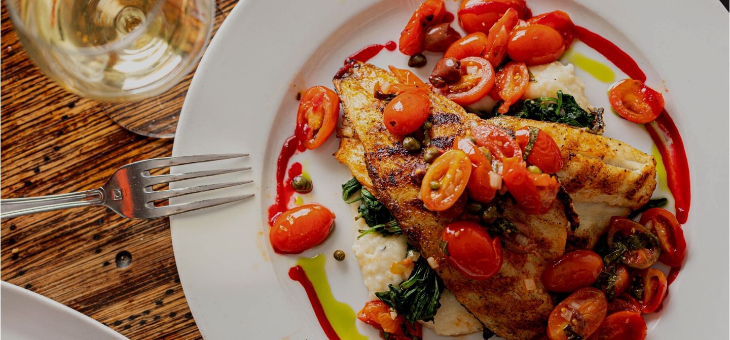Grilled branzino with cherry tomatoes and sautéed spinach on white plate