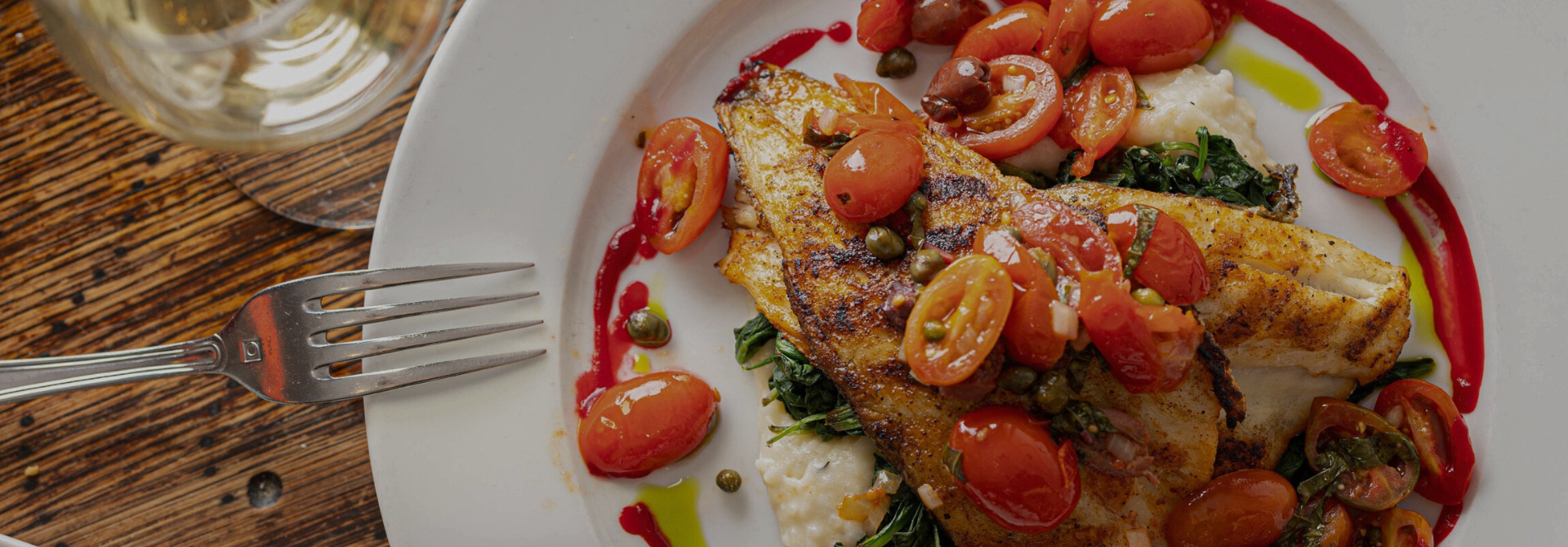Grilled branzino with cherry tomatoes and sautéed spinach on white plate