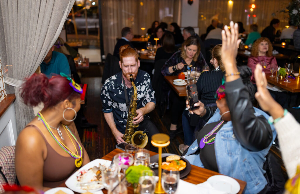 saxophone player at dining table with diners wearing mardi gras masks
